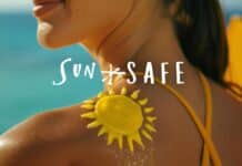 A woman by the beach with a yellow sun design made of sunscreen on her shoulder. The text "SUN SAFE" is written across the image. She is wearing a yellow swimsuit, and the ocean is visible in the background. Stay safe from UV rays with proper sun protection all summer long!