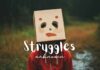 A person stands outdoors wearing a cardboard box over their head with painted eyes, nose, and red mouth. The box has two eye holes. Dressed in a red hoodie, they stand against a blurred natural setting. The words "Struggles unknown" are written in white across the image, reminding us you never know what someone is going through.