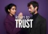 A woman and a man stand facing each other against a purple background, each raising a hand to touch the other's palm. They wear dark, stylish clothing. White text across the center reads, "learn how-to-learn-to-trust.